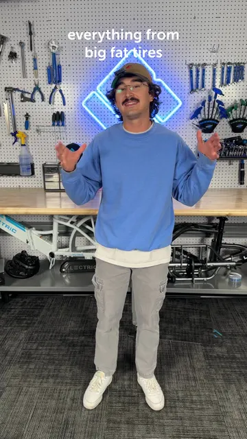 Cover frame of Lectric's tire guide video: a man in a blue sweater talks in front of a tool wall, with the words everything from big fat tires