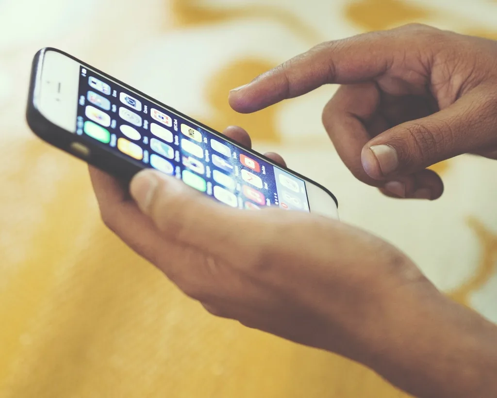 A hand holding a smartphone and swiping upward on the screen with a thumb, the way you move through the TikTok For You feed