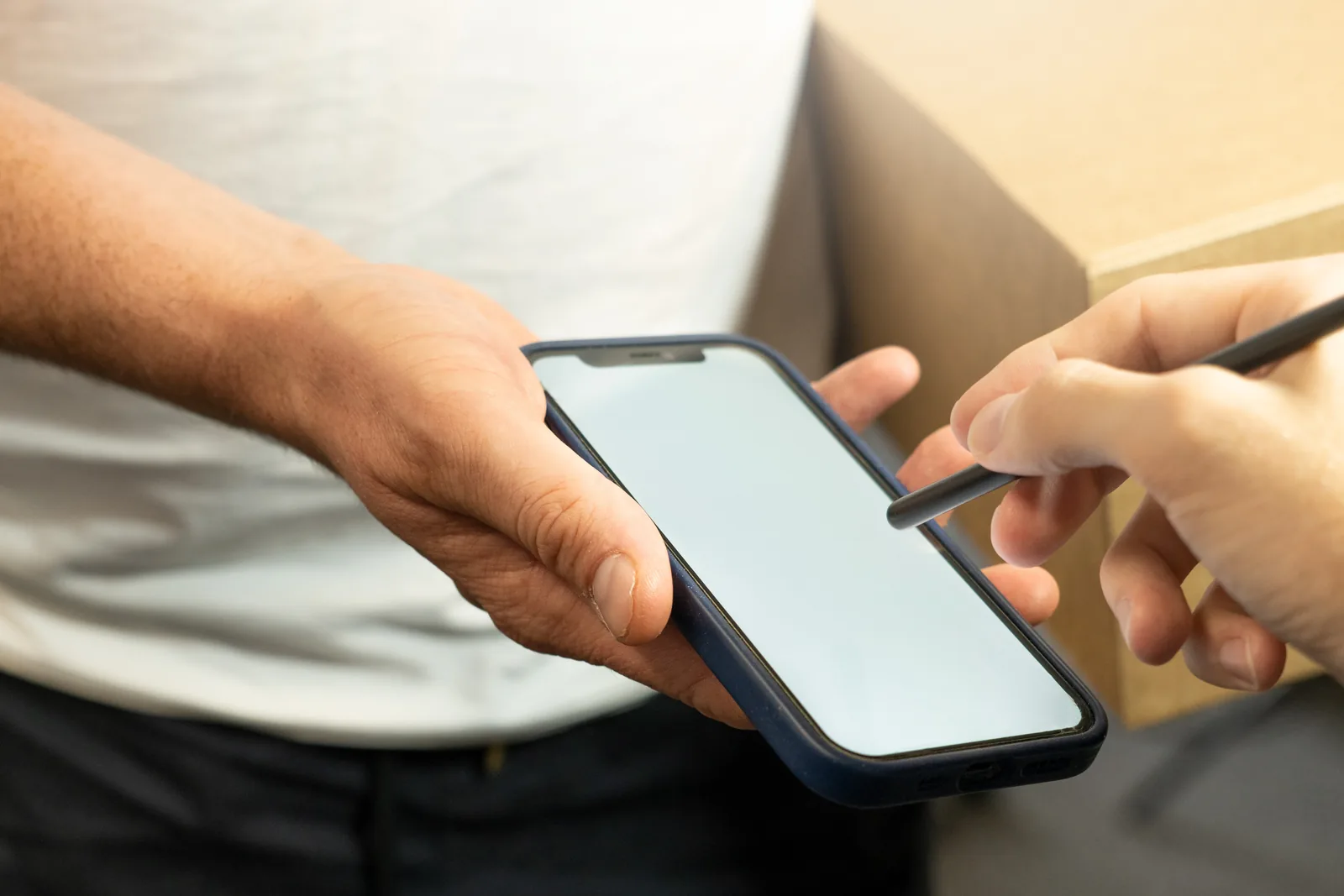 A courier hands over a cardboard parcel while the customer signs for it on a phone screen